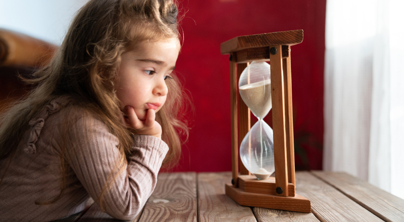 Una niña mira la arena caer en un reloj de arena